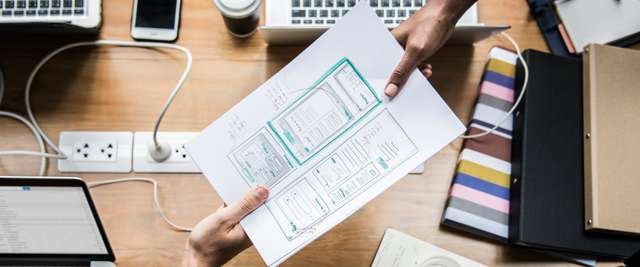 Two people at a desk exchanging a paper that shows Web Design Richmond Hill